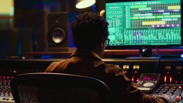 非裔美国人音乐制作人混合和掌握在音频控制台上的曲目 拧旋钮和推动滑块编辑曲调 音响工程师在控制室里创作新歌 相机A — 图库视频影像