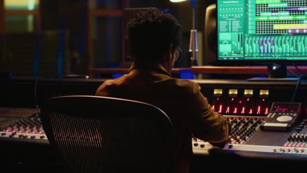 非裔美国人音乐制作人在他的专业工作室的新曲目中探索 在控制室中混音和掌握曲调 技术员按下声卡面板上的按钮和滑块 相机A — 图库视频影像