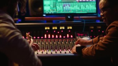 Profesyonel stüdyoda ses mühendisiyle bir şarkı besteleyen söz yazarı, kontrol odasında elektro akustik gitarıyla kayıt yapıyor. Müzisyen, karıştırma konsoluyla şarkılar üretiyor. Kamera A.