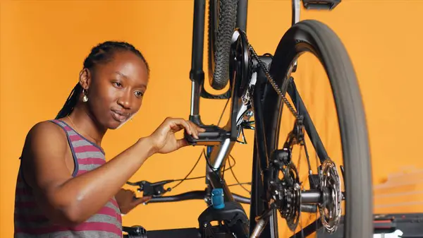 愉快的技师用旋转踏板检查自行车的性能 微笑专家确保自行车轮子上的轮胎在橙色工作室背景下在检查时的正常功能 相机A — 图库照片