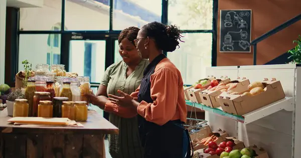 stock image Merchant presenting homemade sauces and spices to client, promoting local farming and healthy eating. Storekeeper recommending bio organic bulk products at supermarket. Handheld shot.