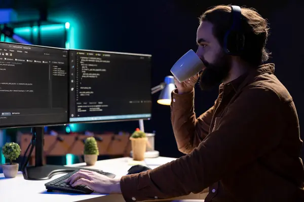 サイバーセキュリティの専門家は 企業のセキュリティ上の脆弱性を模索し マルウェア感染を予防しながらコーヒーを飲んでいます Pcに強化コードをインストールしながらホットドリンクを楽しむプログラマー — ストック写真