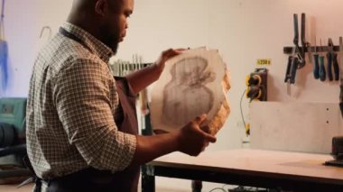 BIPOC çalışanı montaj atölyesindeki odunları teftiş ediyor, koruma ekipmanları takıyor ve raflardan aletleri topluyor. Afrika kökenli Amerikalı marangoz kereste bloğu toplayıp üzerine yığılmaya hazırlanıyor. Kamera A.