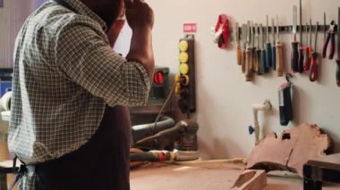 BıPOC marangoz, ahşap atölyesinde mobilya montajından önce kereste parçalarını inceliyor, çizikleri kontrol ediyor. Dolap yapımcısı kereste bloğunu değerlendirir, raftan doğru aracı seçer, kamera A