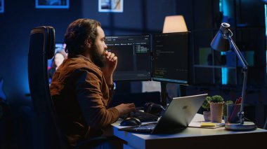 Yazılım uygulaması geliştirmek için Java programlama dilini kullanan geliştirici ev ofisinde kod yazıyor. Görevleri bitirmek için çoklu monitör PC kurulumu ve dizüstü bilgisayar kullanan profesyonel bir sistem. Kamera A
