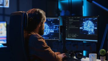 Deneyimli geliştirici yapay zeka sinirsel ağlarını güncellemek için bilgisayar kullanır, merkez ofiste kod senaryoları yazar. Uzaktan çalışan Yapay Zeka simülasyonu modeli A kamerasını güncellemek için programlama kullanır.