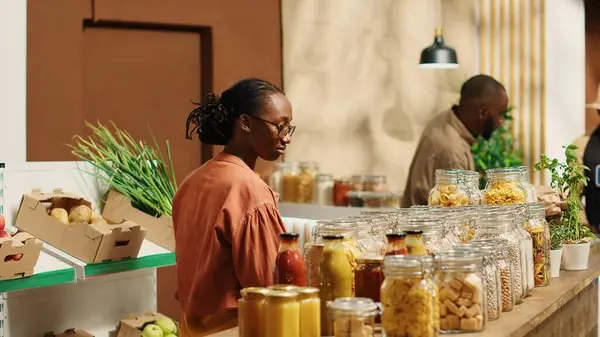 stock image African american client examines bio homemade bulk products, looking to buy natural ethically sourced food alternatives for healthy nutrition. Woman shopping for goods at zero waste store. Camera 1.