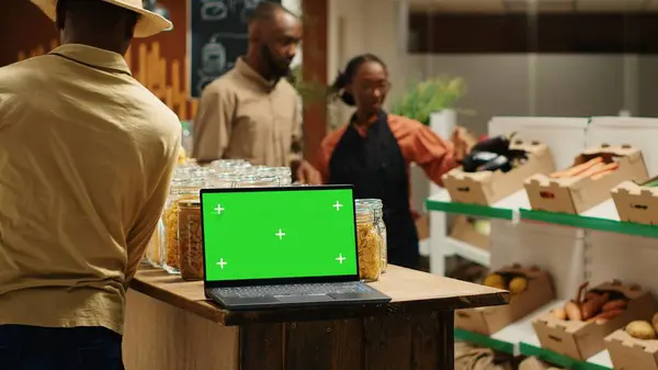 stock image Laptop on stall at supermarket showing greenscreen template, people shopping for organic homegrown products in zero waste eco store. Portable pc with blank chromakey and copyspace. Camera 1.