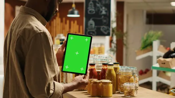 stock image African american client holding tablet with greenscreen layout in local organic shop, looking at chromakey next to additives free goods. Regular customer uses device with isolated copyspace. Camera 1.