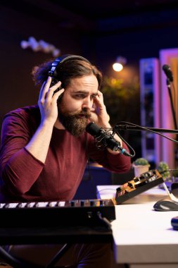 Genç ses mühendisi kulaklıkları ses kaydı yapmak için kullanıyor, mikrofonda şarkı söyleyerek daw yazılım arayüzündeki müziği düzenliyor. Yetenekli yapımcı karıştırma konsolunda ses parçaları oluşturuyor.