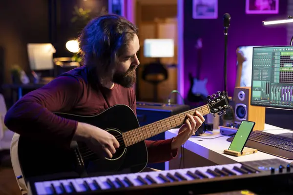音乐家在智能手机绿屏旁边弹奏乐器 学习新的弦乐协奏曲来弹奏吉他 艺术家在家里的工作室里发展他的音乐技巧 — 图库照片