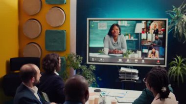 Proje yönetimi ekibi hissedarlarla yapılan video görüşmesine katılarak güncellemeleri ve veri raporlarını gözden geçirmek üzere bir sunum hazırlıyor. Çalışanlar yönetim kurulu üyeleriyle uzaktan tartışıyor. Kamera B.