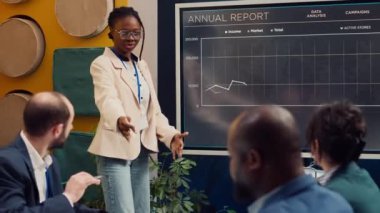 Bir durum güncelleme toplantısında bilgi sunan pazarlama asistanı, anahtar performans göstergeleri oluşturmak için veri araştırması yapıyor. Etkileşimli yönetim kurulunda çalışan Afrikalı Amerikalı bir çalışan. Kamera A.