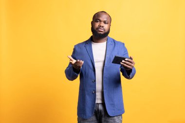 Arkadaşından kötü haber aldıktan sonra hayal kırıklığına uğramış bir adamın portresi. Akıllı telefondan konuşuyor. Üzücü BIPOC çalışanı, telefondaki mesajları okuduktan sonra kaşlarını çatıyor.
