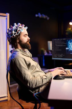 Man with EEG headset on typing on keyboard, writing code allowing him to transfer mind into computer virtual world. Transhumanist closing eyes, transcending, becoming one with AI clipart
