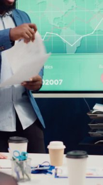 Proje yöneticisi yönetim kurulu ofisinde yönetim kurulu ekibiyle görüşerek, görevlerini etkileyebilecek düzenleyici değişikliklere ilişkin güncellemeleri inceliyor. Lider paylaşımı kağıtlar üzerinde analiz yaptı. Kamera A.
