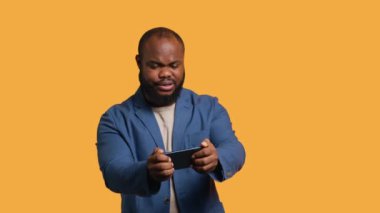 BIPOC çalışanı akıllı telefondan video oyunu oynuyor, yenilgiden sonra negatif duygu patlaması yaşıyor. Hüsrana uğramış oyuncu telefonda oyunu kaybediyor, stüdyo arka planında izole edilmiş, kamera A