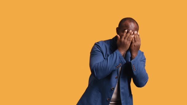 アフリカ系アメリカ人男性は スタジオの背景で認識されるのを避けるために手で顔を覆っています 誰かから隠れて苦しんでいるBipocの人 顔の前に手のひらを置く カメラB — ストック動画
