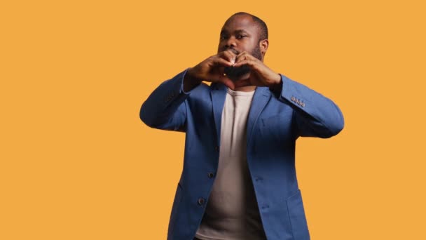 一个快乐友善的非洲裔美国人的画像 用手做心形手势 愉快地养育Bipoc的人表现出爱心的姿态 隔离在工作室的背景上 摄像头B — 图库视频影像