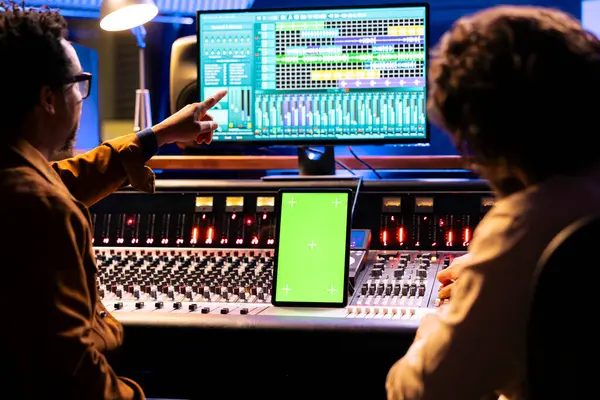 艺术家和音响工程师在平板电脑上与绿屏显示一起工作 并用音频控制台和数字软件混合和掌握曲目 音乐家团队编辑音乐 机动爱好者 图库图片