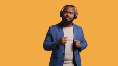 Mutlu Afro-Amerikan vatandaşı, kulaklıkla elektronik şarkılar dinleyip eğleniyor. Neşeli BIPOC DJ gibi davranıyor, dans müziğinden hoşlanıyor, stüdyo arka planı, kamera B