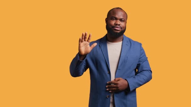 アフリカ系アメリカ人男性は さよならを言って挨拶の手のジェスチャーをすることに消極的だった 悲しいBipocの人物の肖像画は スタジオの背景 カメラBの上に孤立した後に誰かに挨拶するために腕を上げる — ストック動画