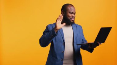 Telekonferans toplantısında iş arkadaşlarını laptopla karşılamak, stüdyo geçmişi. Gülümseyen işçi el sallıyor, internette iş arkadaşlarını selamlıyor, kamera B
