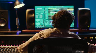 Müzik yapımcısı, kontrol odasında ses yazılımı ve karıştırma konsolu ile bir parça bitiriyor, sesleri işlemek için profesyonel stüdyoda teknik ekipmanlarla çalışıyor. Ses teknisyeni iş başında. Kamera A.