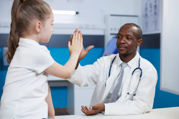アフリカ系アメリカ人医師は 病院の診療室で診察中に5歳から子供に高く与える 病気の症状を説明する実験室のコートを持つ黒人男性 医療処置を議論 — ストック写真