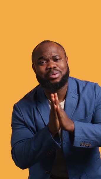 垂直ビデオ アフリカ系アメリカ人男性が手を組んでジェスチャーを乞い 願いを叶え イエロースタジオの背景に隔離されました 何かを求めているBipocの人 祈りと希望 カメラB — ストック動画