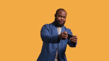 BIPOC çalışanı akıllı telefondan video oyunu oynuyor, yenilgiden sonra negatif duygu patlaması yaşıyor. Hüsrana uğramış oyuncu telefonda oyunu kaybediyor, stüdyo arka planında izole edilmiş, kamera B