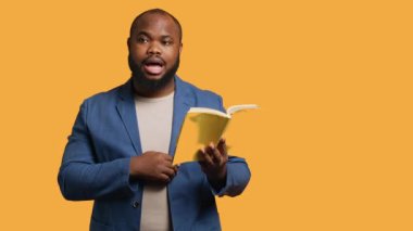 Afrikalı Amerikalı hatip yüksek sesle kitap okuyor, izleyiciler için hikaye anlatıyor. BIPOC çalışanı edebiyat romanı sunuyor, sayfaları okuyor, seyircileri eğlendiriyor, stüdyo arka planı, kamera A