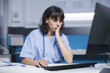 Ofiste, tıbbi asistan sağlık sistemi için bir bilgisayar ve fare kullanıyor. Hemşire gece geç saatlere kadar çalışırken destek ve yardım için monitör ekranına bakıyor..