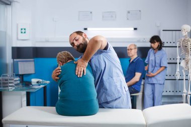 Sertifikalı kinezi uygulayıcısı yaşlı hastaya kas esnemesi ve omurilik baskısı konusunda yardım ediyor. Fizik tedavi sırasında sırt ağrısına yardımcı olan tıbbi asistan..
