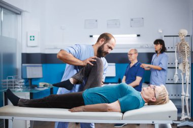 Doktor, ortopedi değerlendirmesi için ortak sorunları olan emekli bir kadına yardım ediyor. Doktor, dizinden yaralanan ve eklem iltihabı tedavisi gören yaşlı bir hasta üzerinde kayropraktik egzersiz yapıyor..