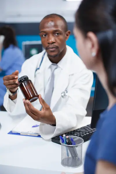 アフリカ系アメリカ人の医師が 医薬品のボトルを持っている間 コカシア人女性に診断と治療を説明した 医療相談を受ける女性患者 ストック画像