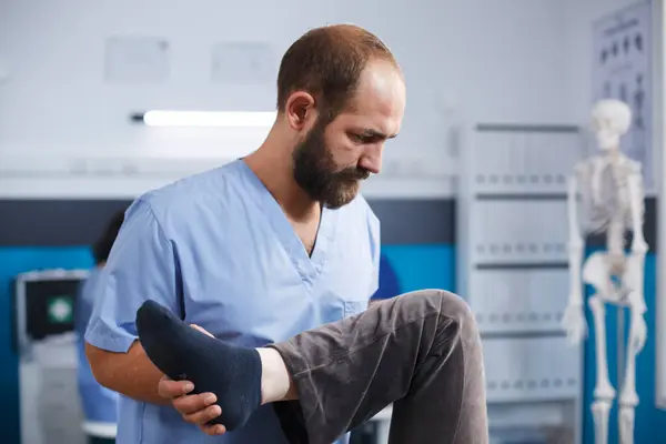为协助老年膝伤患者康复 为脊医提供近距离诊疗服务 老年人在医疗辅助人员的帮助下进行腿部运动 以进行骨病理学治疗 图库照片