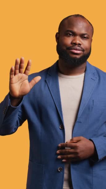 垂直ビデオ アフリカ系アメリカ人の男性は さよならを言って挨拶の手のジェスチャーを行っています 悲しいBipocの人物の肖像画は スタジオの背景に孤立した後に誰かに挨拶するために腕を上げます — ストック動画
