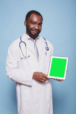 Steteskop ve laboratuvar önlüğü giyen siyah bir adamın portresi yeşil ekranlı bir tablet tutuyor. Boş kromakey model şablonu gösteren Afrika kökenli Amerikalı doktor kavrama aygıtı.