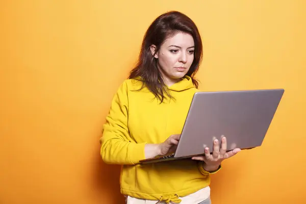 stock image Female freelancer utilizing modern technology by using digital laptop. Portrait of focused woman working online on wireless computer while standing over isolated orange background.