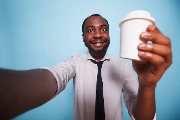 黑人男子有一个视频电话 同时拿起一杯咖啡与孤立的背景 身穿白衬衫的非洲裔美国人微笑着 手里拿着酒瓶拍了一张自拍照片 — 图库照片