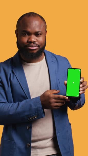 垂直ビデオ アフリカ系アメリカ人男性が グリーン スクリーンの携帯電話を 持つジェスチャーを示しています スマートフォン スタジオのバックグラウンドに関する拒絶手のジェスチャーをしているBipocの人 ストック映像