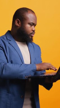 Şirket adına iş yapmak için dizüstü bilgisayar kullanan dikey Afrikalı Amerikalı bir adam stüdyo arka planında izole edilmiş. Bütçe, tahmin ve finansal analizler yapan bir ofis çalışanı