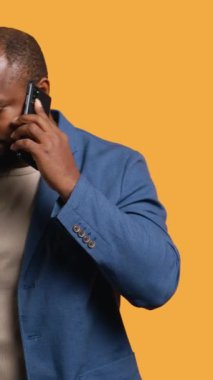 Pozitif duyguları olan dikey videolu neşeli adam, telefon görüşmesinde arkadaşlarıyla konuşmaktan keyif alıyor, akıllı telefon kullanıyor, stüdyo geçmişi kullanıyor. Gülümseyen mutlu insan, telefonda iyi haberler alıyor.