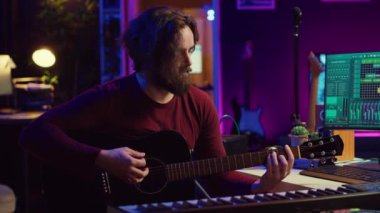 Erkek söz yazarının portresi akustik gitar çalıyor ve ev stüdyosunda müzik sesi kaydediyor. Dijital sesli çalışma istasyonu yazılımı ile melodiler bestelemek. Kamera A.