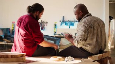 BIPOC sanatçısı ve çırağı dizüstü bilgisayardaki CAD yazılım 3D ile ahşap sanat eseri şemasını karşılaştırıyor. Stüdyo çapraz çizim uzmanları not defteri taslağı, kamera B