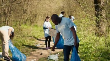 Afrikalı Amerikalı gönüllü çöpleri ve maşalarla plastik atıkları toplamaya çöp öğütücüsünde çöp toplamaya ve geri dönüşüm yapmaya gönüllü. Orman kirliliği ve yasadışı çöplükle mücadele eden aktivist. Kamera A.