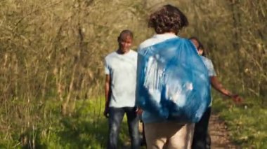 Üretken bir temizlik oturumundan sonra ormandaki çöpleri ve plastik atıkları temizlemede başarılı olan insanlar ormanı terk ediyor. Mutlu gururlu eylemciler. Kamera A.