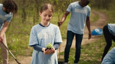 Sevimli çocuk eylemcisi elinde küçük bir tohum ağacı sunuyor, çevreyi ve doğal ekosistemi korumak için savaşıyor. Doğayı korumak ve ağaç dikmek için çalışan küçük bir kız. Kamera A.