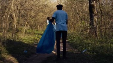 Afro-Amerikalı bir kız çöp torbasında maşa kullanarak çöp topluyor, plastik atıkları geri dönüştürüyor ve ormandaki çöpleri topluyor. Ormanı çöpten temizleyen genç bir kadın eylemci. Kamera B.